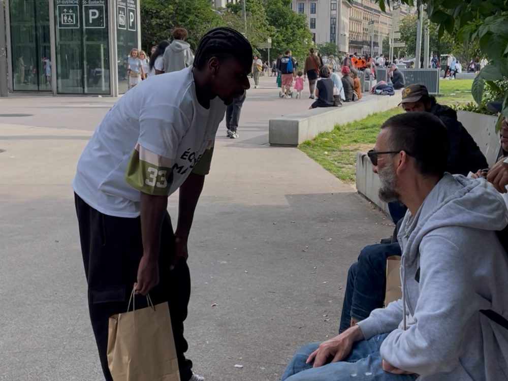 Un bénévole discute avec un homme assis sur un banc, aux Halles