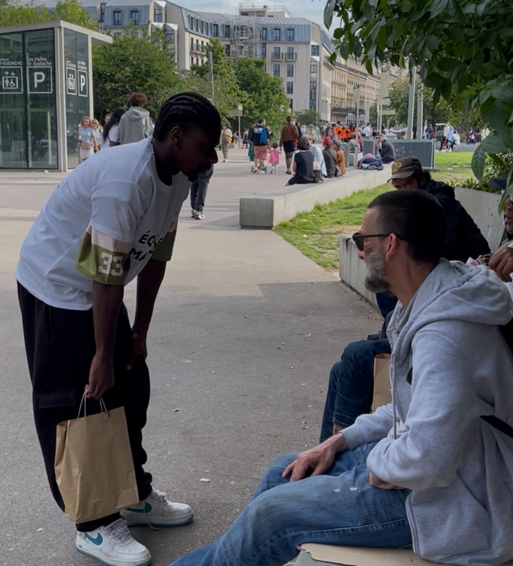Un bénévole discute avec un homme assis sur un banc, aux Halles